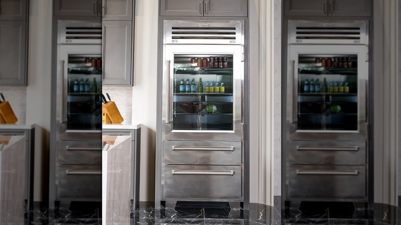 A stainless steel Sub-Zero refrigerator with glass window set into grey cabinetry.