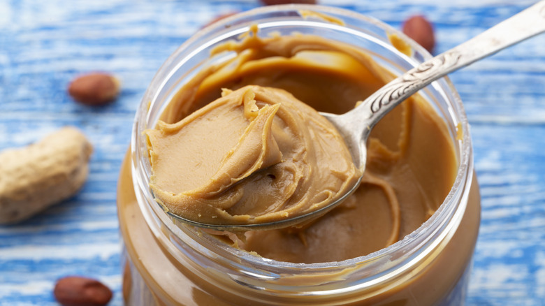 A spoon full of peanut butter sits atop a peanut butter jar