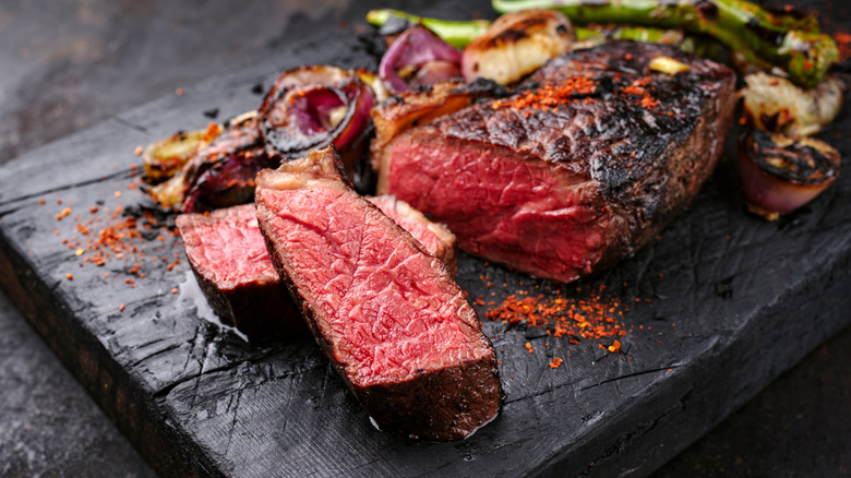 Aged steak sliced up on a black cutting board.