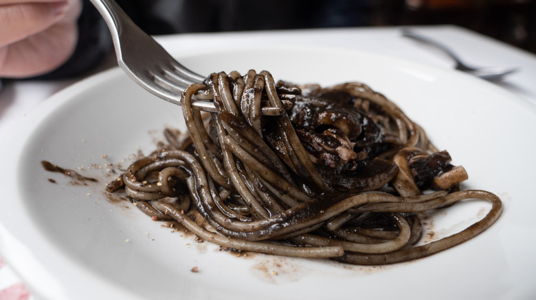 Person twirling squid ink spaghetti with fork