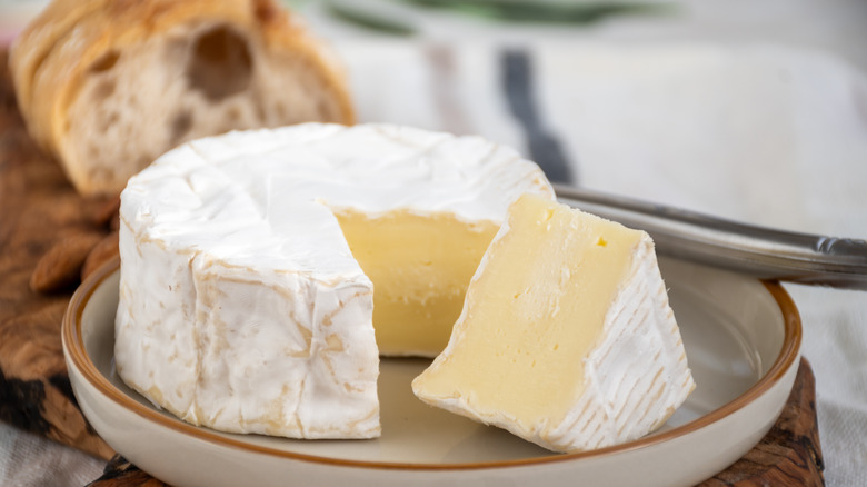 Wheel of Camembert cheese with slices taken out and sliced bread in the background