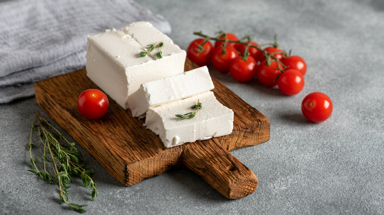 Wooden cutting board with Feta, fresh tomatoes, and rosemary sprigs