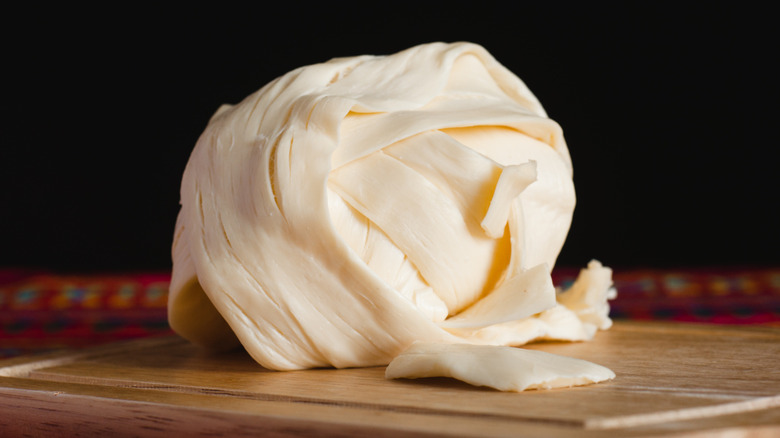 Rolled chunk of Oaxaca cheese on a wooden cutting board