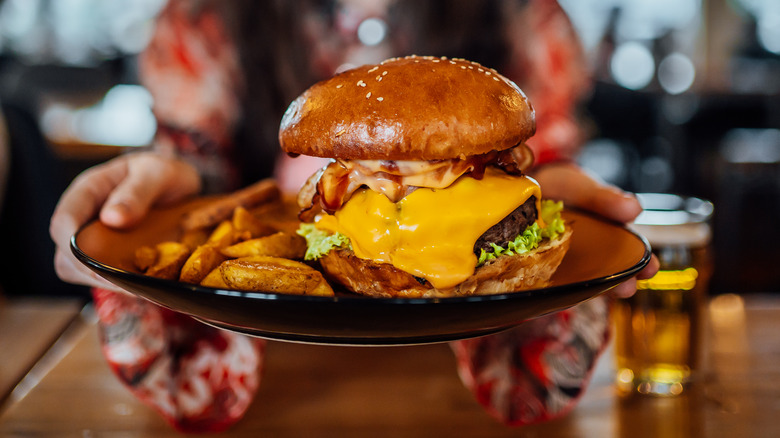 Woman holding plate of cheeseburger in potato bun