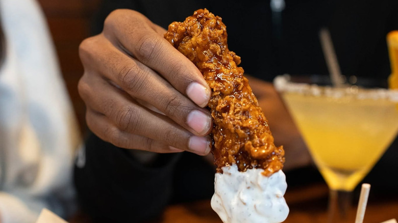 A hand holding one of Chili's sauce-covered Chicken Crispers dipped into ranch.