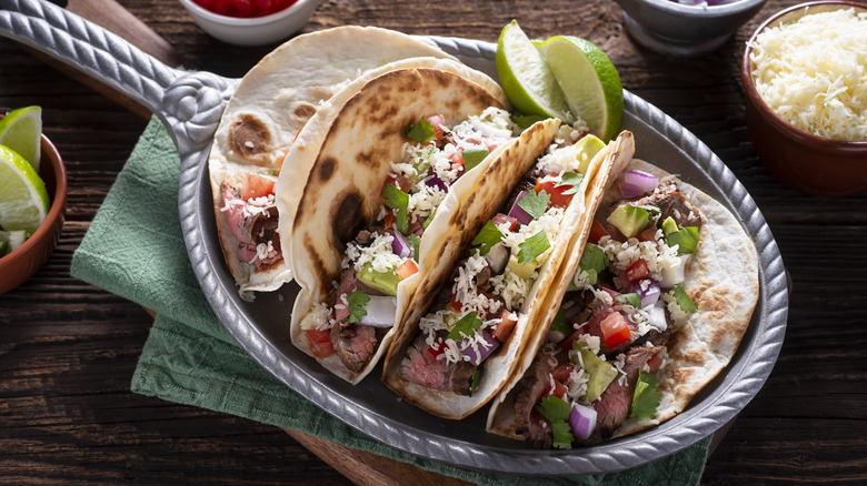 Steak tacos on a silver serving basket on a wooden table