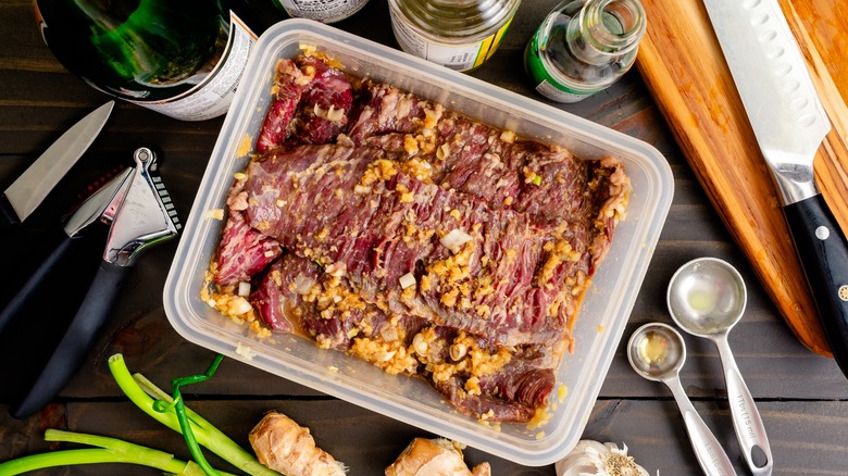 Skirt steak marinating in a plastic container on a table
