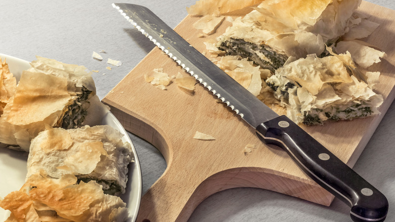 serrated knife on cutting board with spanakopita