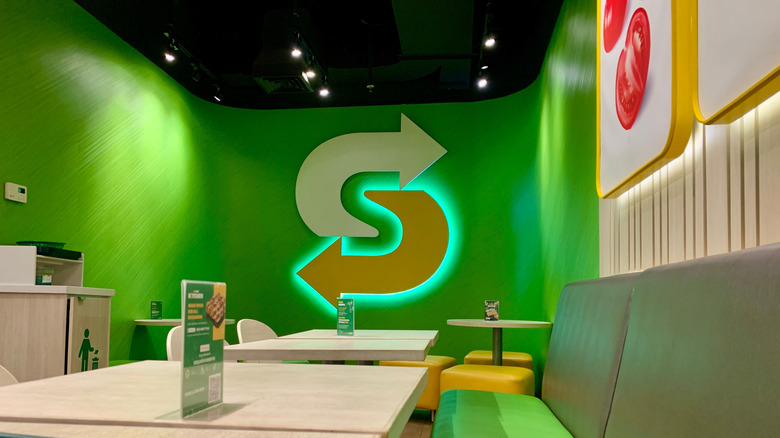 A Subway logo sign gleams green inside a restaurant