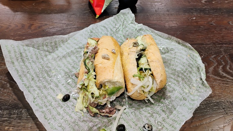 A Publix sub sandwich sits on its wrapper on a wooden table