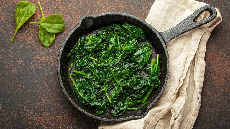 Steamed spinach in a cast iron pan over a folded cloth napkin
