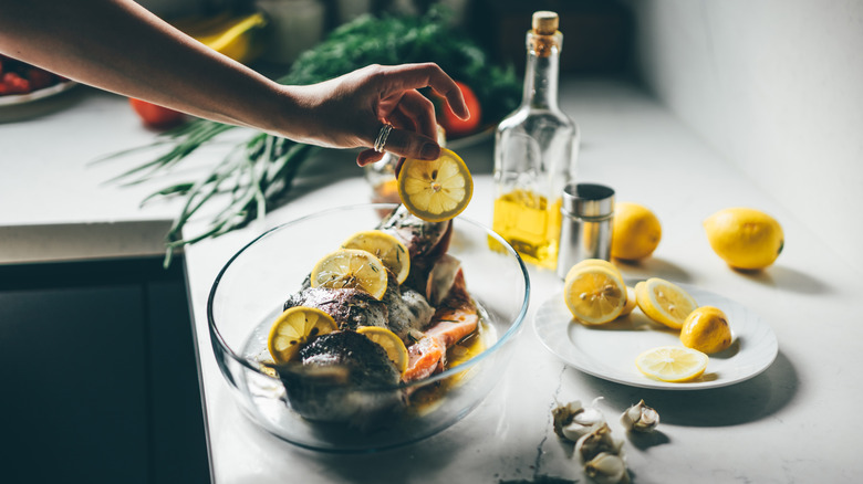 Hand placing lemon slices in a dish with a whole fish