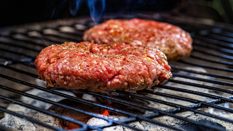 Two hamburger patties on a grill, seasoned simply with salt and pepper