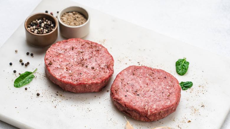 Two steakburger patties sit on white slab, with little bowls of salt and pepper nearby