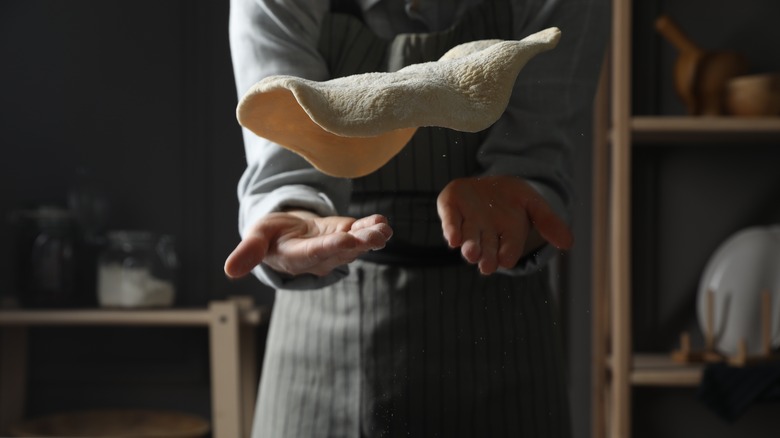 Person tossing pizza dough in the air.
