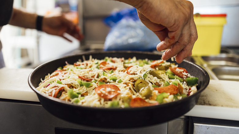 Person putting toppings on deep dish pizza.