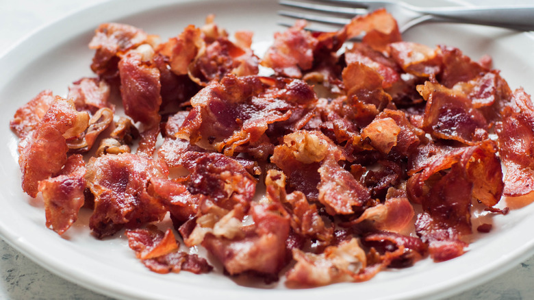 Strips of crispy bacon on a white plate with a fork