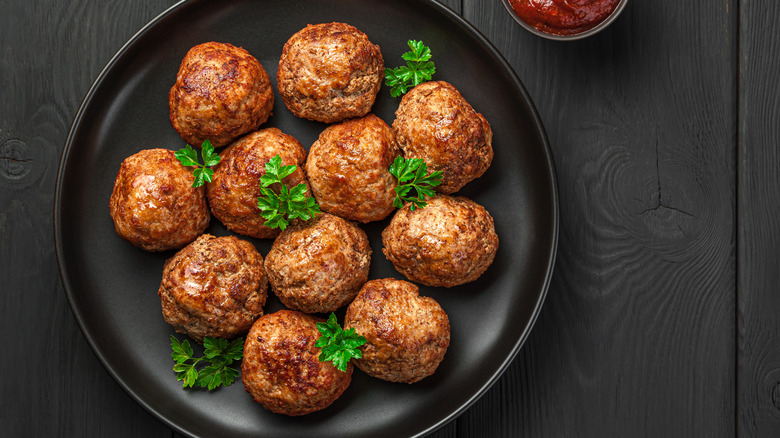 A bowl of meatballs has fresh parsley speckled throughout it.