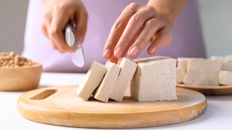 A person is slicing tofu on a cutting board