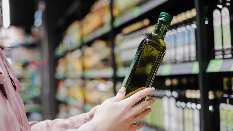 A shopper picks up a bottle of olive oil in a grocery store