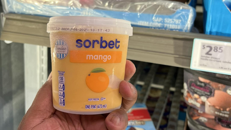 A hand holds up a pint of Aldi's mango sorbet