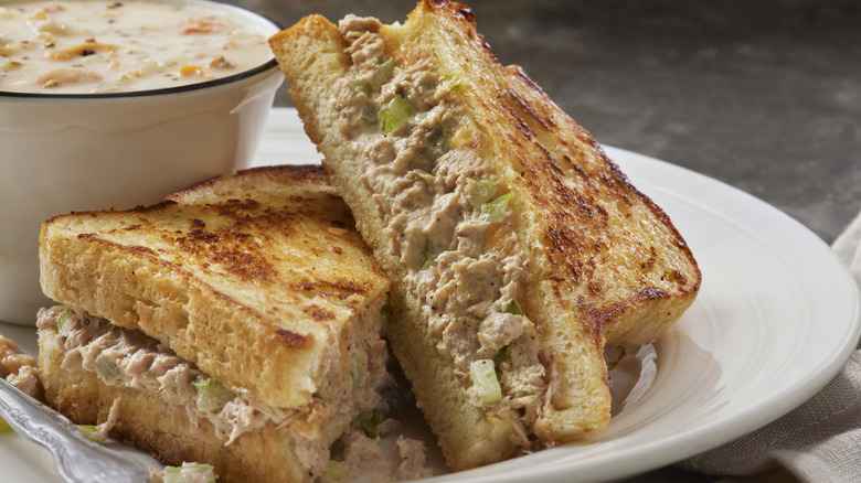 A tuna melt, perfectly toasted and sliced in half, sits next to a bowl of warm clam chowder