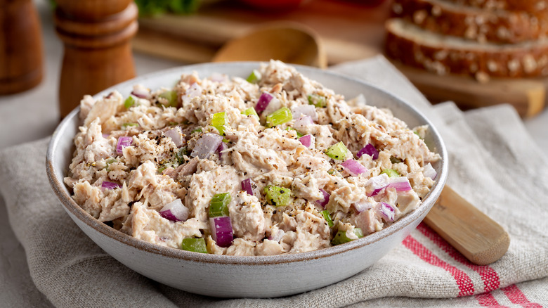 A bowl of tuna salad on a kitchen cloth with slices of bread in the background
