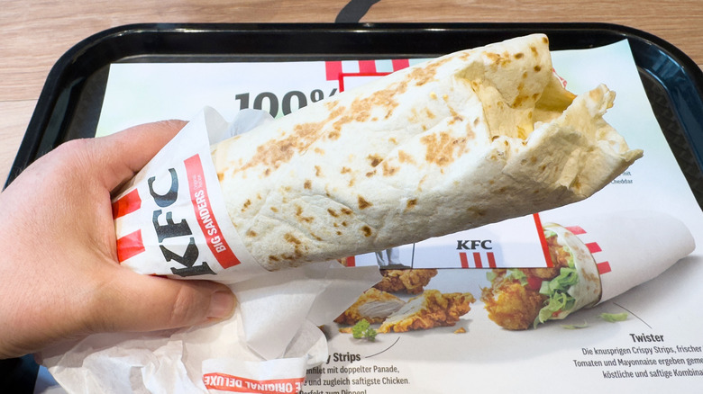 Hand holding a KFC wrap atop a restaurant tray