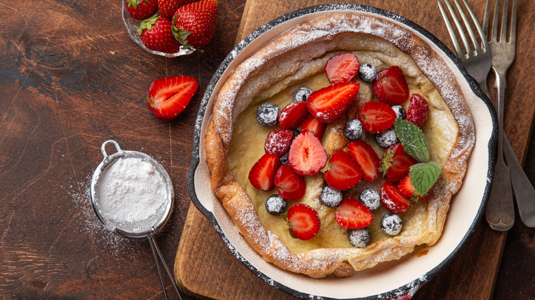 Dutch baby pancake in skillet with berries and sugar
