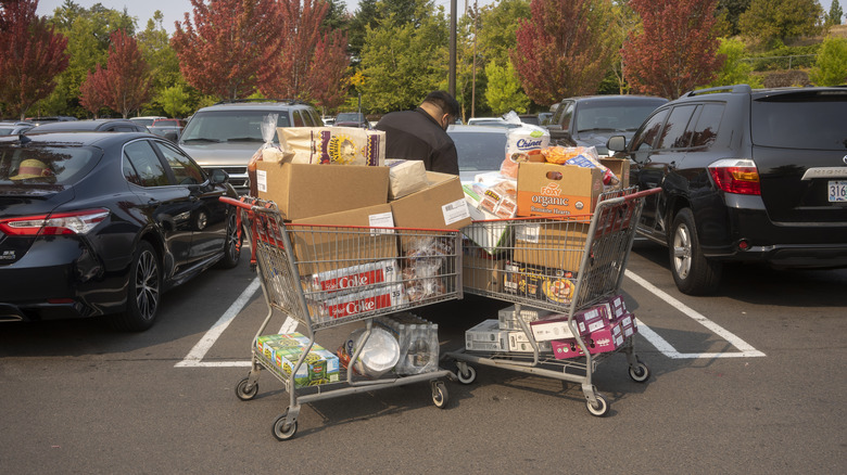 A man with two full Costco carts opens his trunk in the parking lot