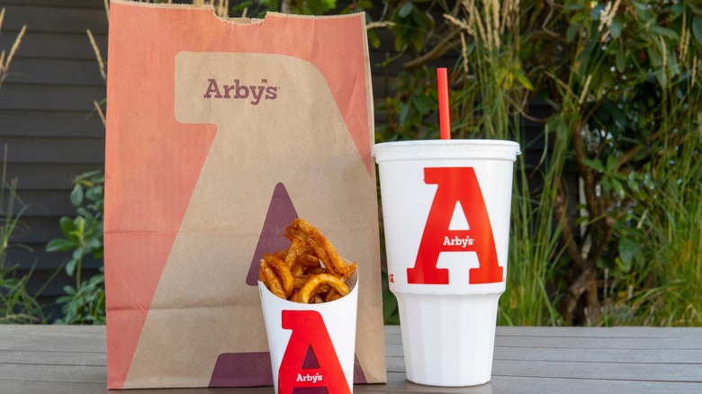 An Arby's takeout bag with a side of curly fries and a large fountain drink