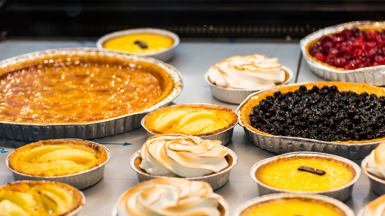 A variety of pies sit in their aluminum pans on a table