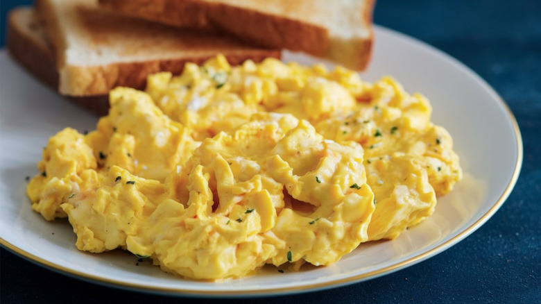 Soft scrambled eggs on a white plate with stacked pieces of toast