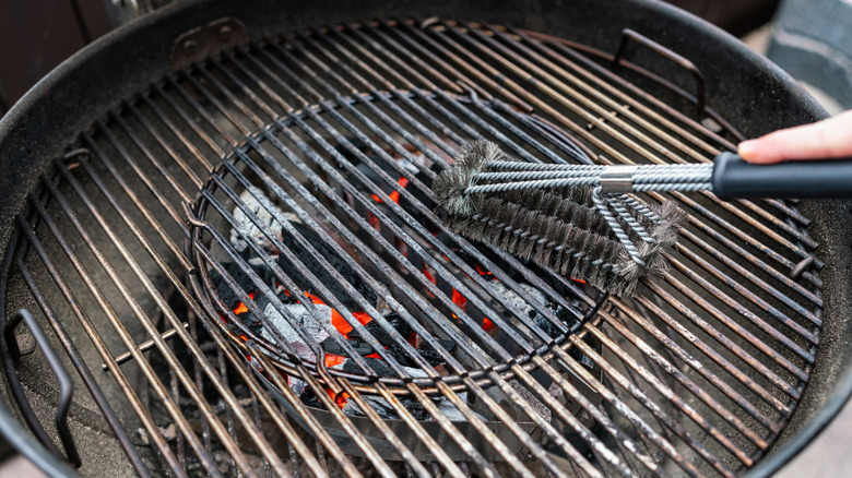 Cleaning a hot charcoal grill grate with a wire brush.