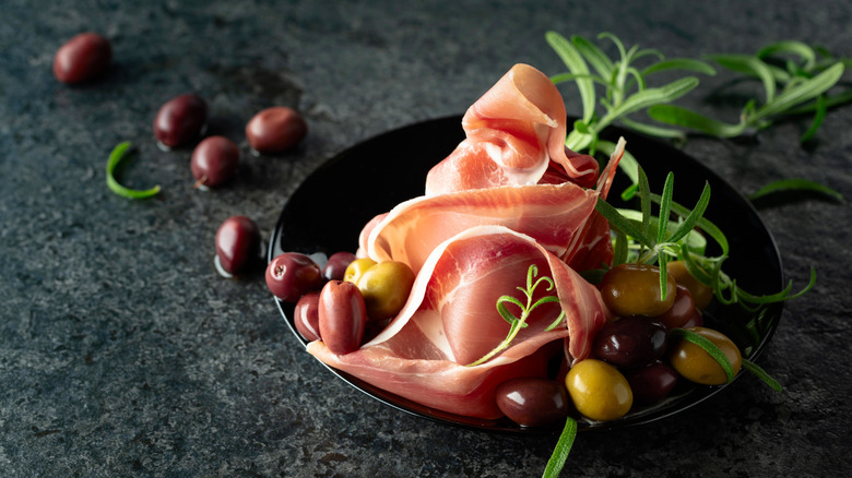 A bowl of prosciutto crudo with olives and herbs