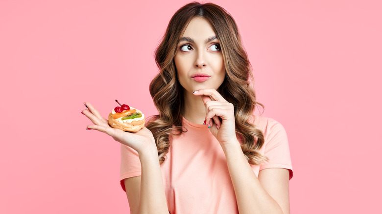 A person, looking pensive and uncertain, holds a fruit tart.