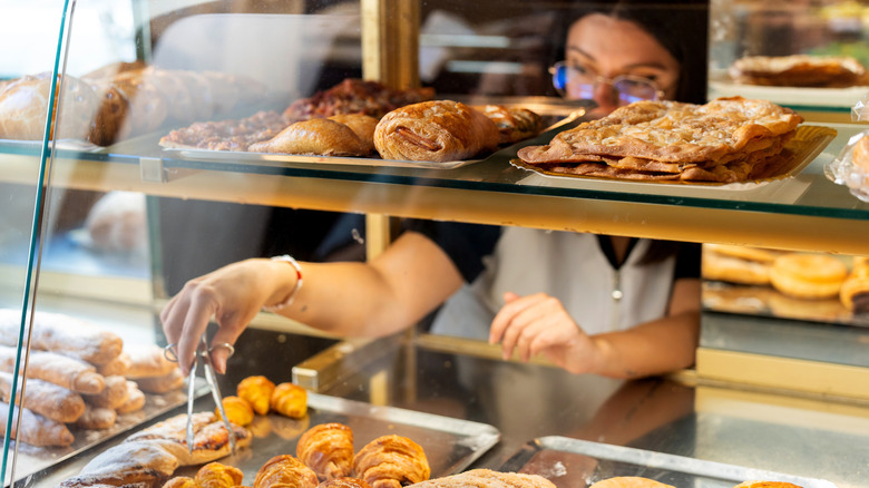 A bakery worker uses tongs to remove a pastry from a display case.