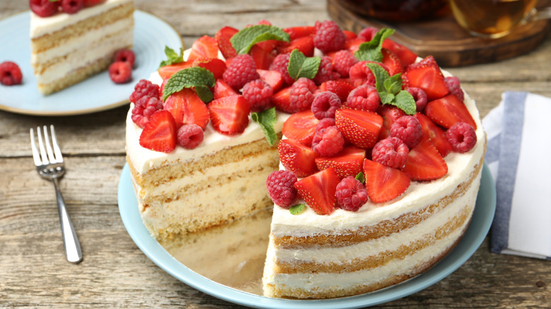 A layered sponge cake topped with cream and a multitude of strawberries, raspberries, and fresh mint