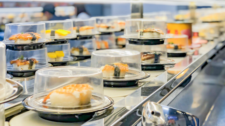 covered sushi dishes on conveyer belt