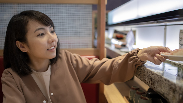 Person taking sushi plate off conveyor belt