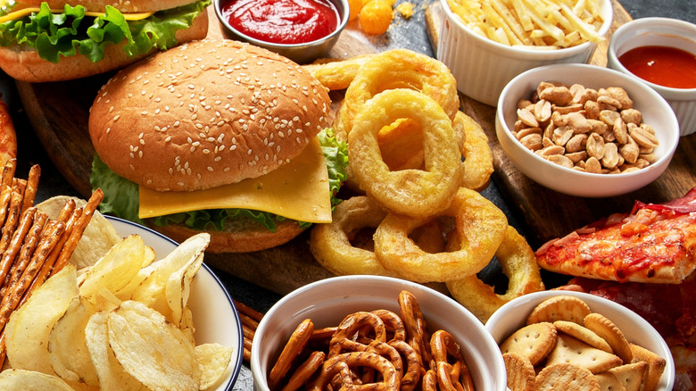 a spread of American dishes, from burgers and chips to onion rings, peanuts, pretzels, crackers, and pizza