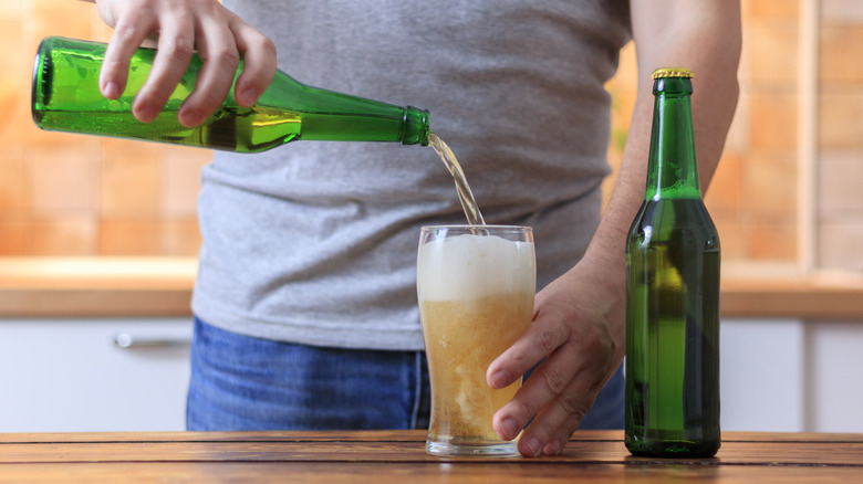 pouring open bottle of beer into glass on kitchen counter