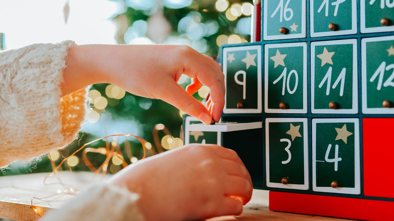 A child's hands open a window in an advent calendar