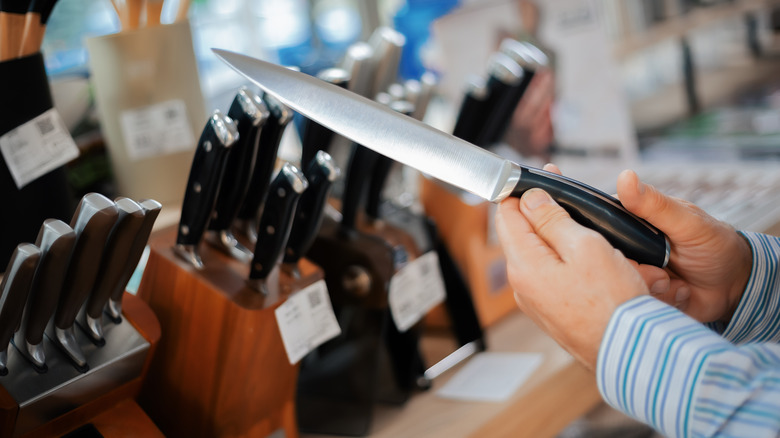 Someone examining a knife in front of some knife sets