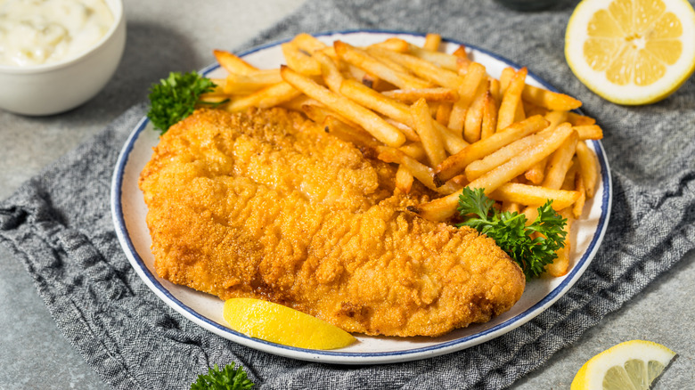 Pristine plate of fried catfish served with fries, lemon, and tartar sauce.