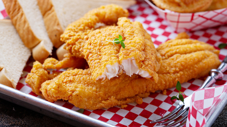 Plate of fried catfish with bread in the background.
