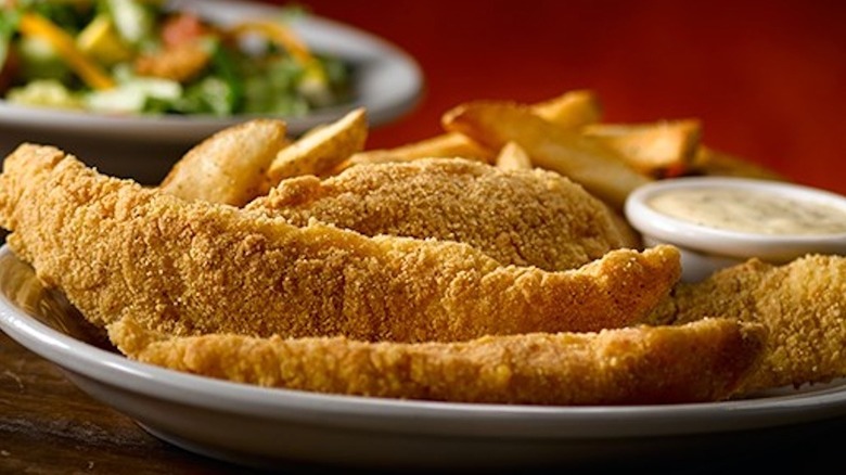Platter of Texas Roadhouse catfish sitting on a plate with sauce.