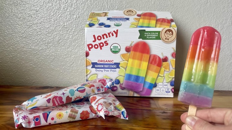Hand holding an unwrapped Jonny Pops Organic Rainbow Fruit Stack with the box in the background