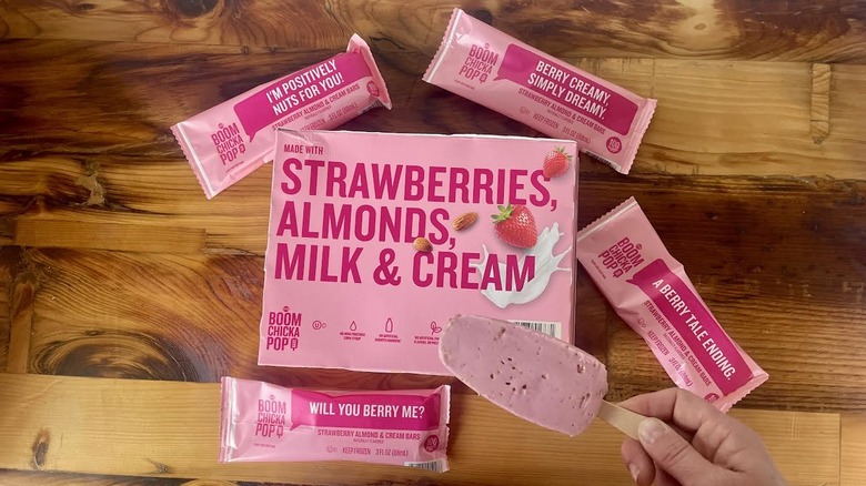 Overhead view of a box of Boom Chicka Pop Strawberry, Almond & Cream Bars with a hand holding an unwrapped one