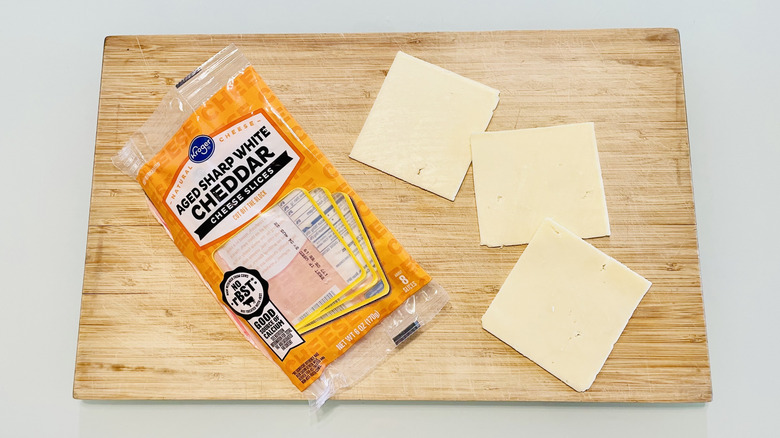 Slices of Kroger Aged Sharp White Cheddar Cheese with a grilled cheese sandwich